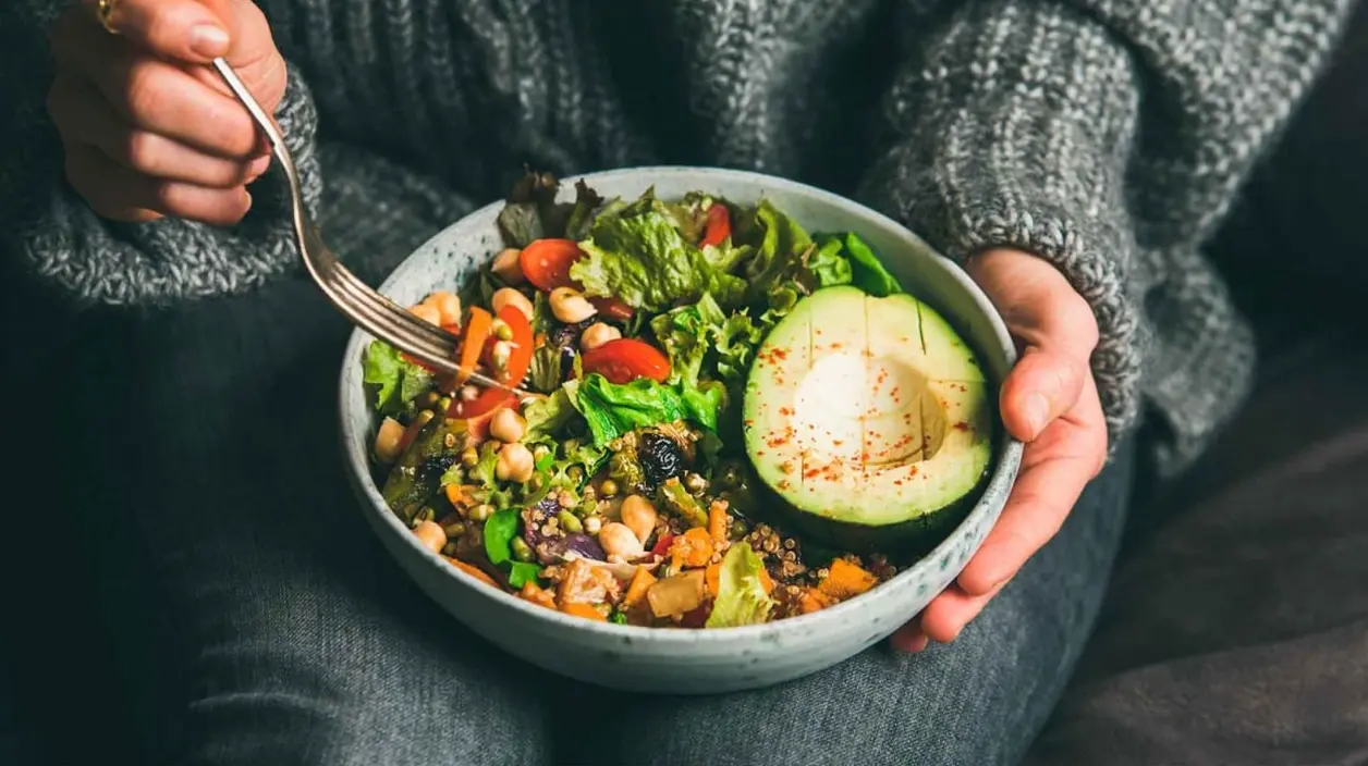 Mujer come un bol de ensalada con aguacate, garbanzos y verduras