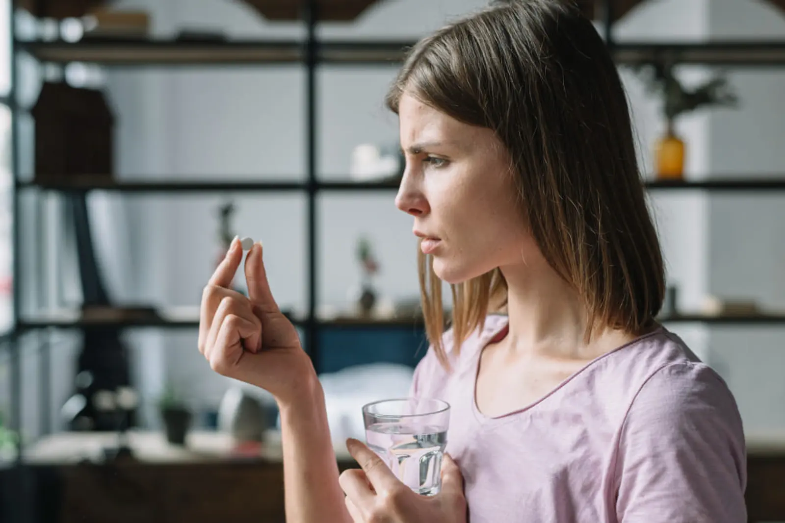 Mujer de perfil observa una pastilla mientras sostiene un vaso de agua
