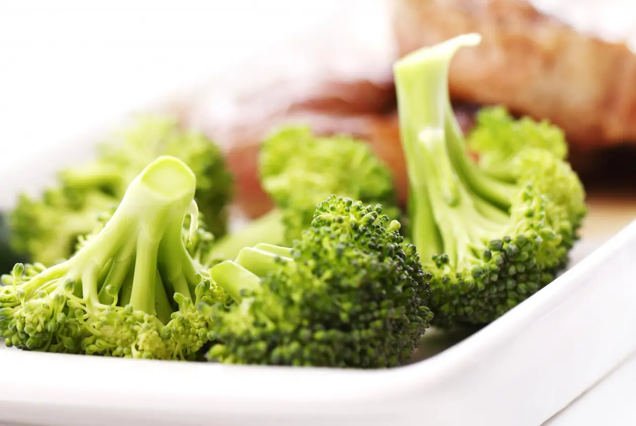 Primer plano de ramilletes de brócoli cocido en un plato blanco