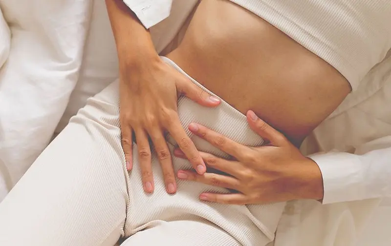 Mujer en pijama blanco con las manos sobre el bajo vientre