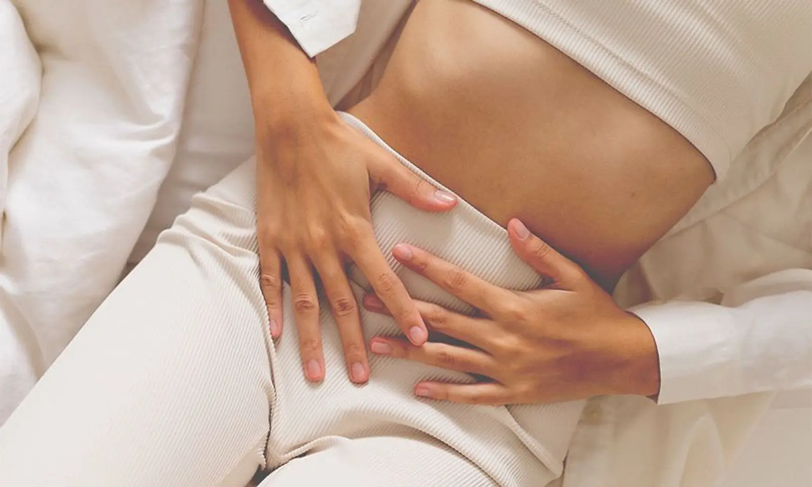 Mujer en pijama blanco con las manos sobre el bajo vientre