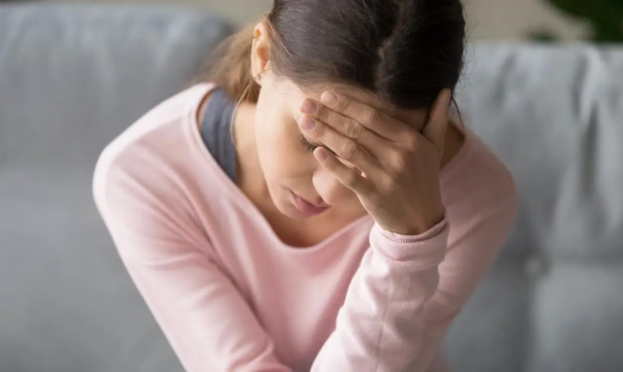 Mujer se lleva la mano a la frente con gesto de agobio sentada en el sofá