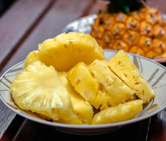 Plato de piña troceada con una piña entera al fondo