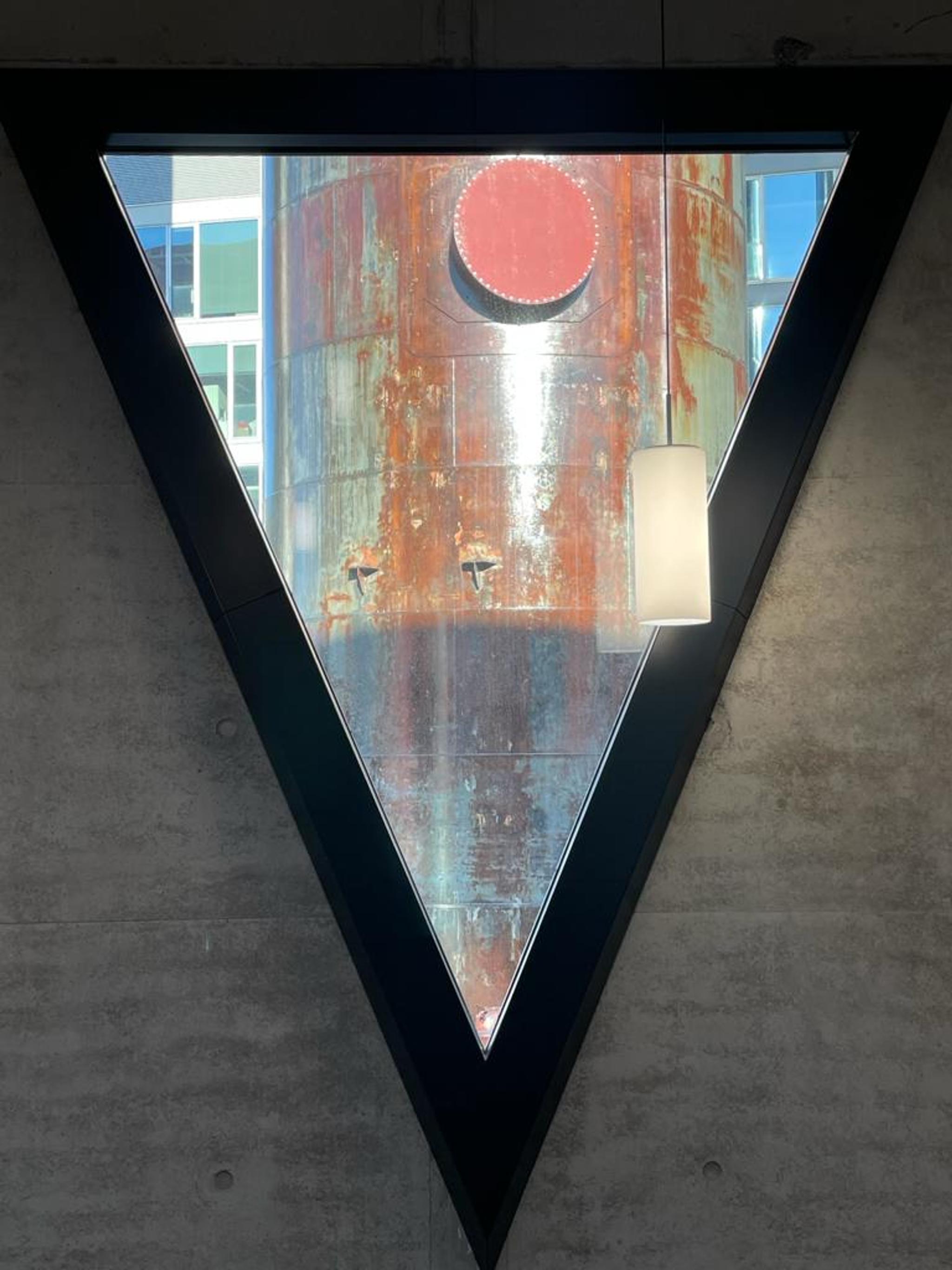A metal industrial tube is seen through a triangular window with a black frame.