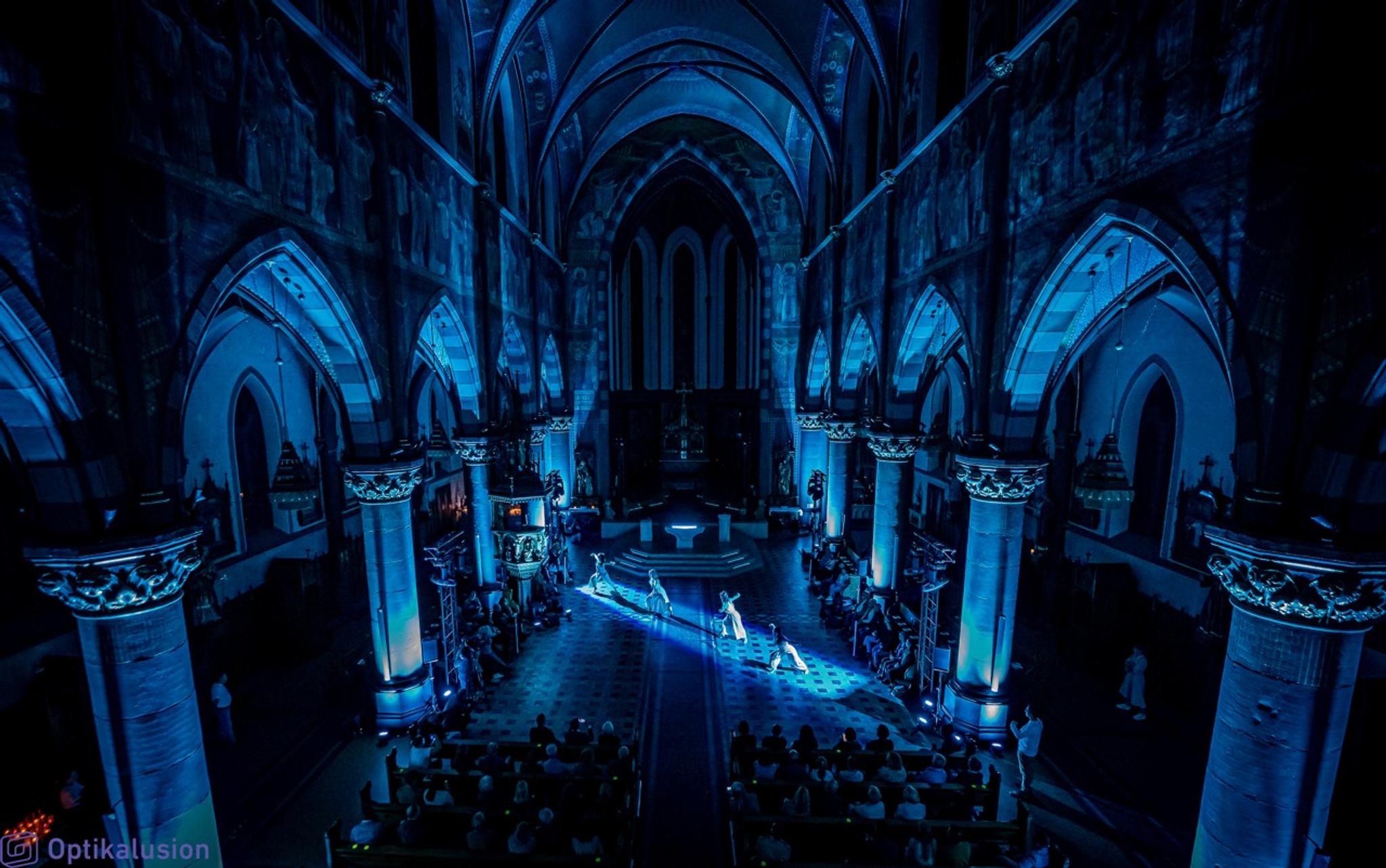 Dancers perform in a blue lit cathedral