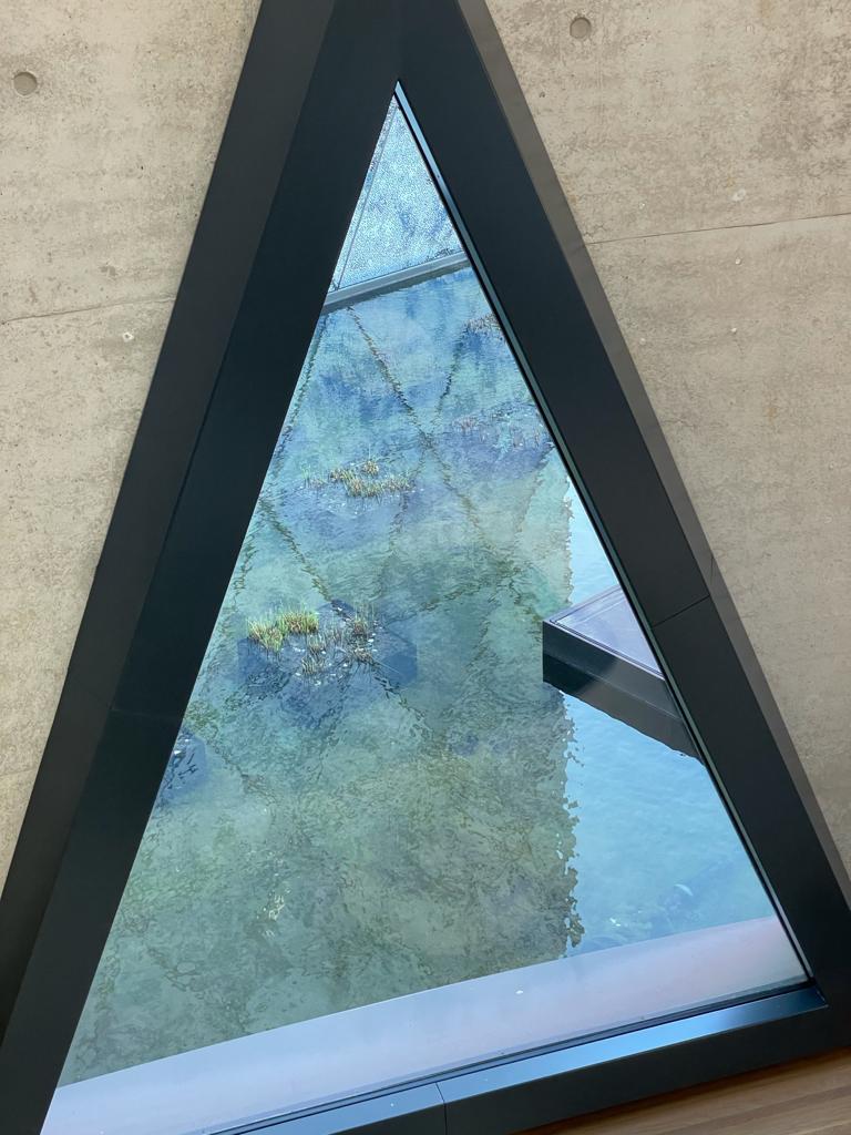 A pond reflecting the marble wall is seen through a triangular window with a black frame.