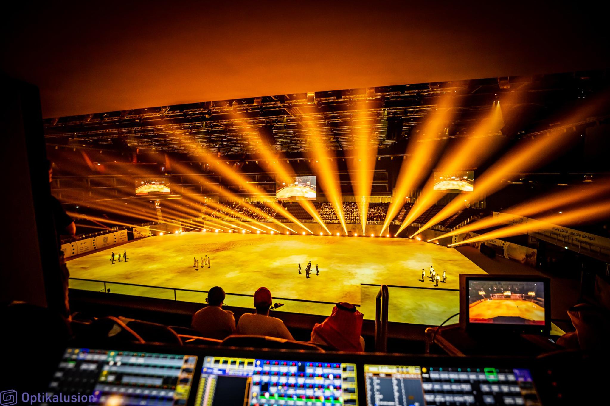 An indoor arena as seen from the tech booth. Beams of orange spotlights emit from the ground.