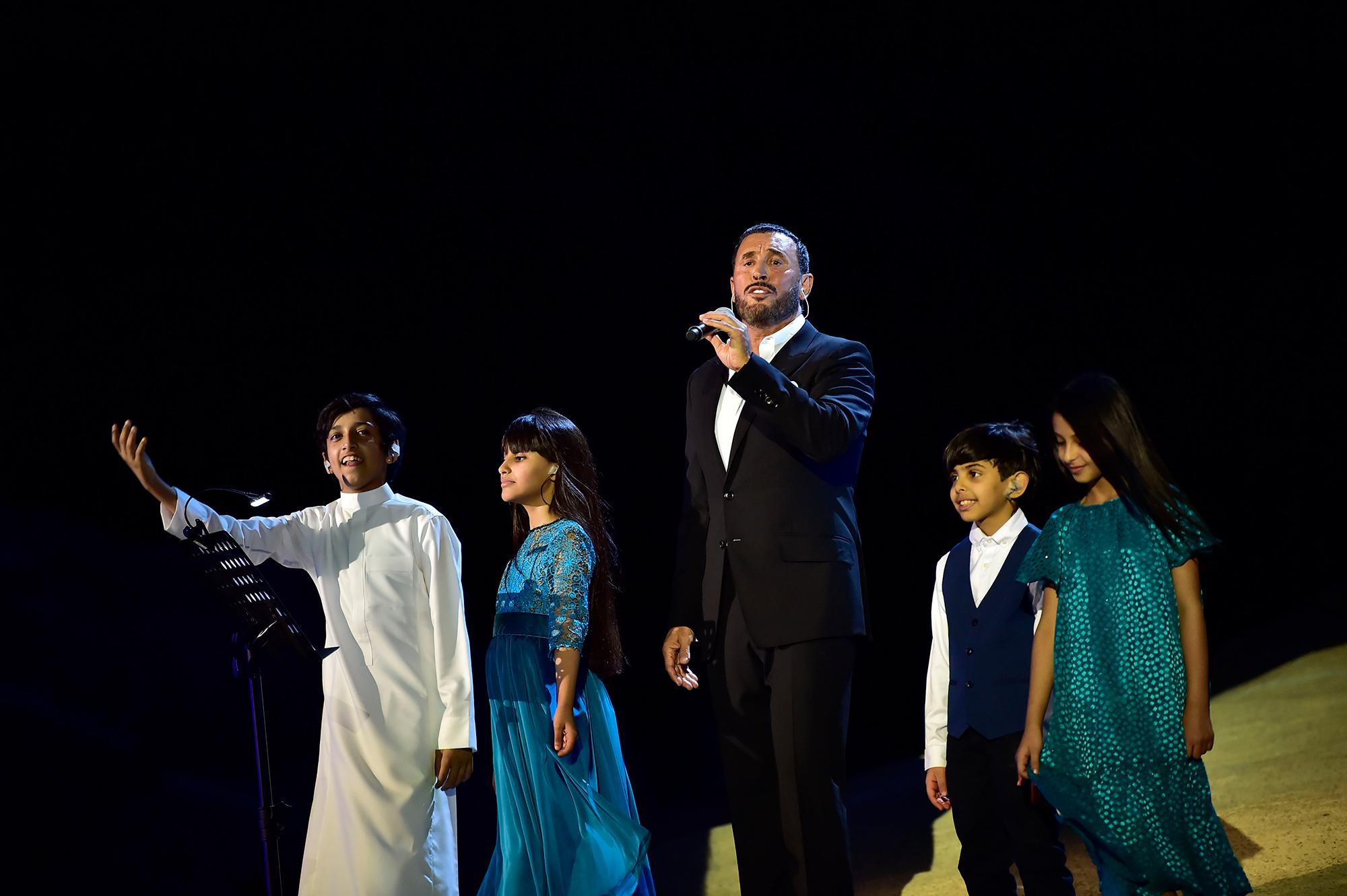 A singer performs with 4 children around him.