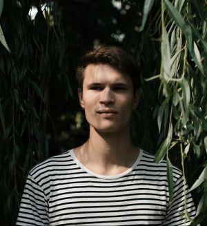 Electronic music producer Alex.Do stands under a willow tree.