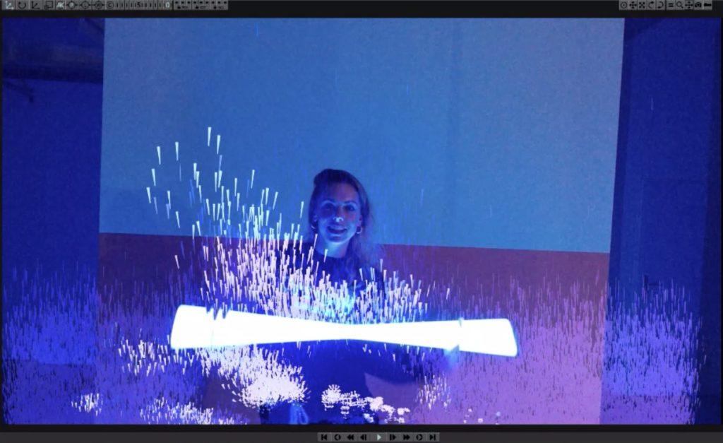 Computer screen with a woman holding a bright tube of light. There are flecks of light digitally emanating from it.