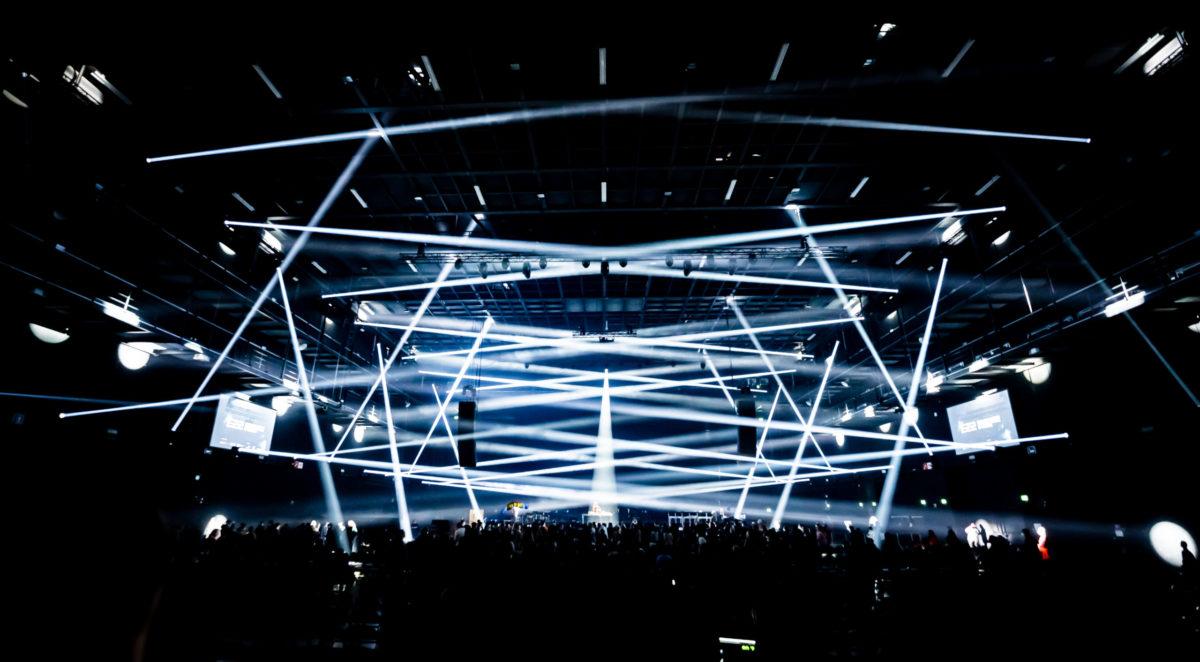 The light show for Future Frequencies criss crosses over a large crowd. There are tunneled beams of white light overlapping over one another.