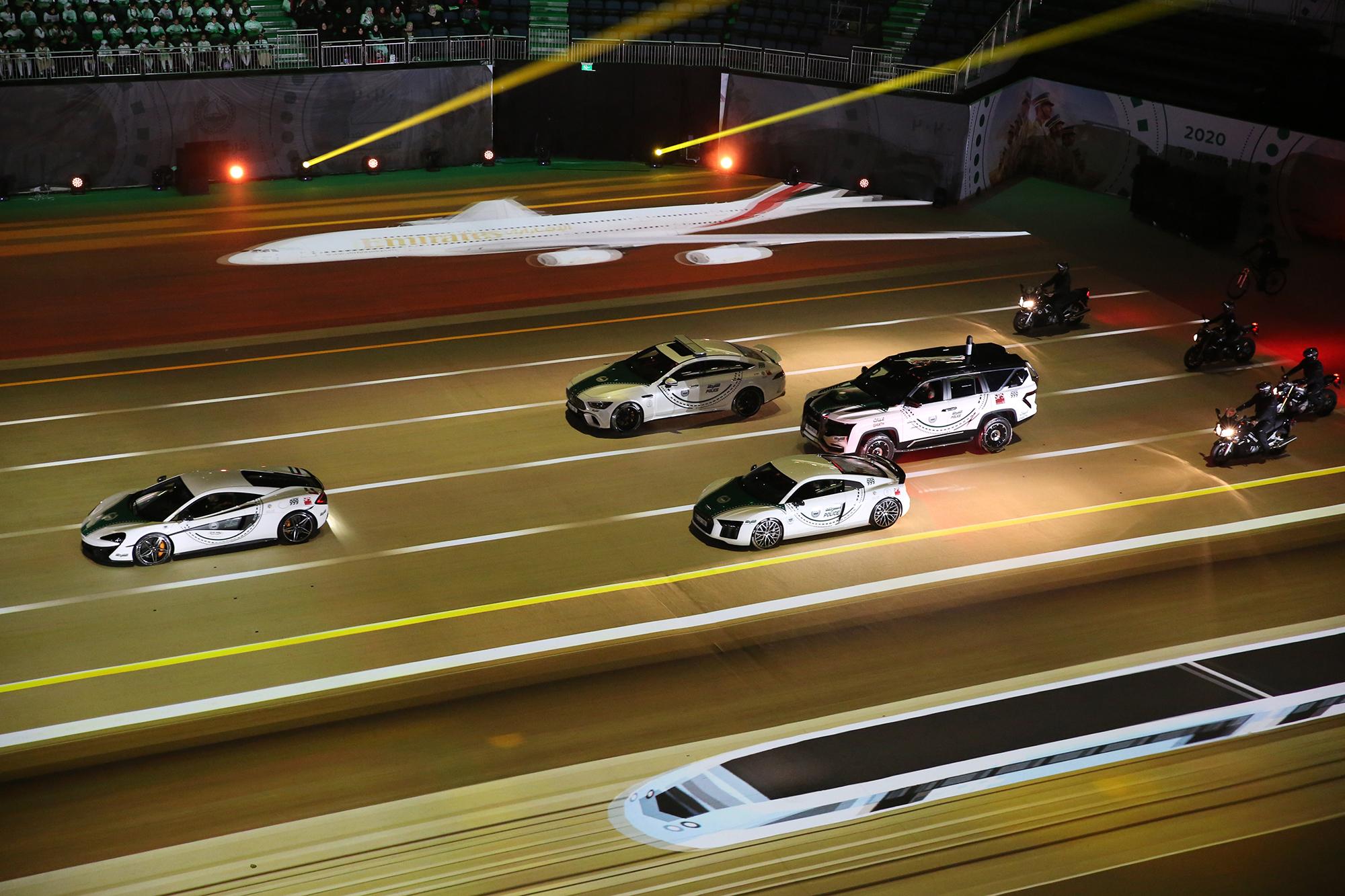 Physical cars and motorcycles drive in the arena on top of projection mapped content.