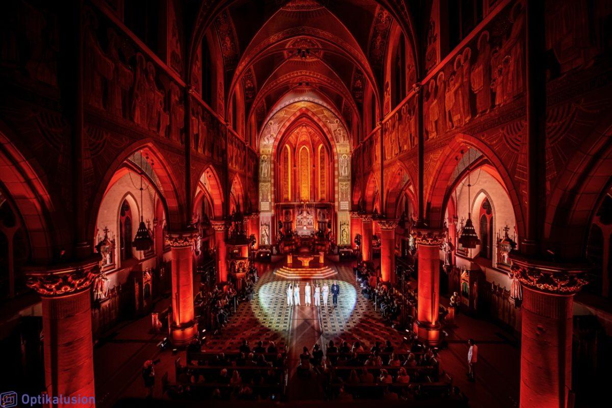 Dancers perform in a red lit cathedral