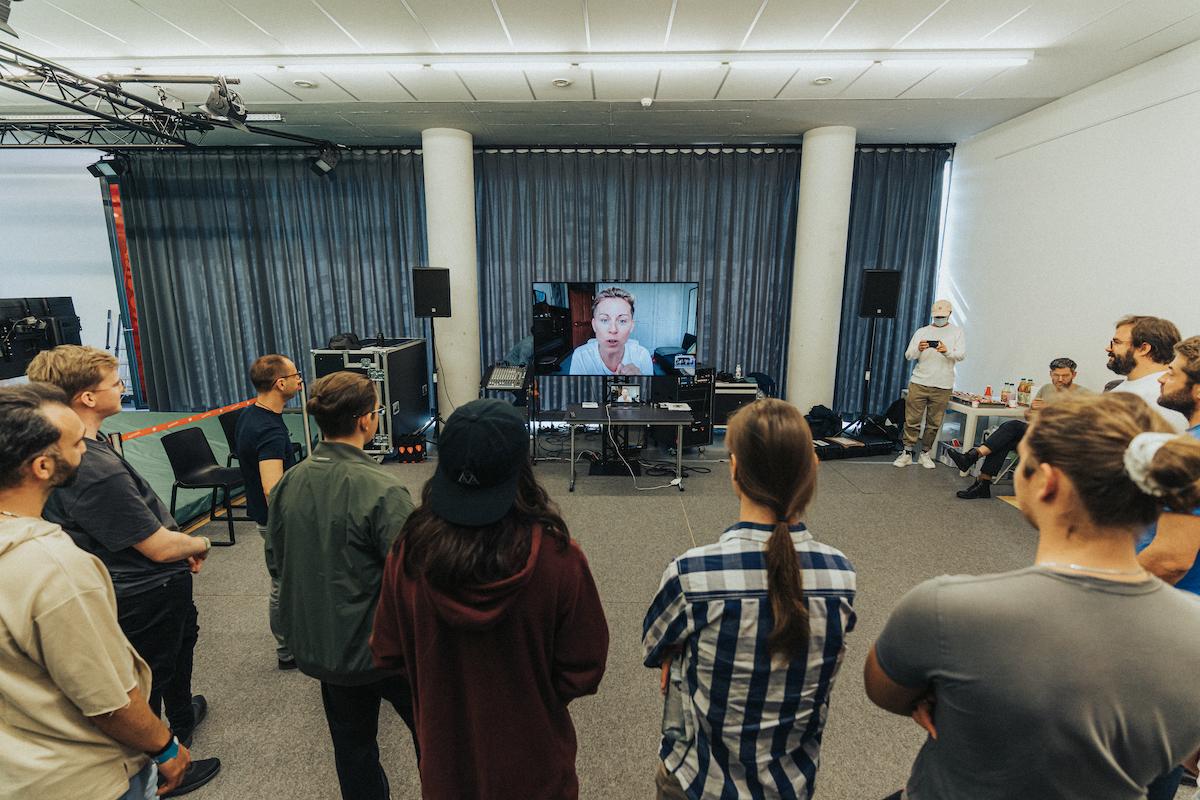 A workshop group look at a monitor with someone's face on it.