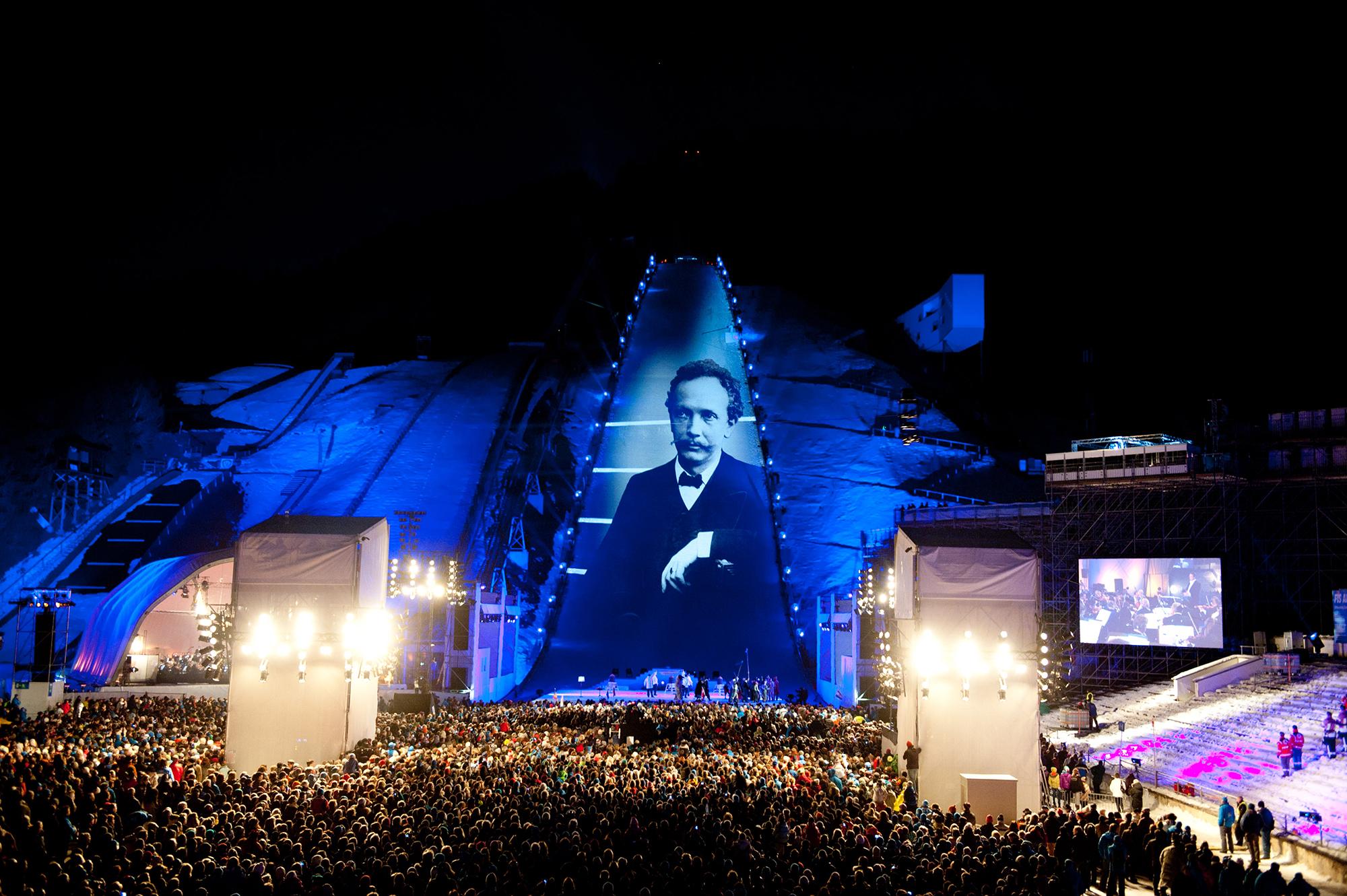 An old photo is projection mapped onto the ski slope as a sea of people looks on.