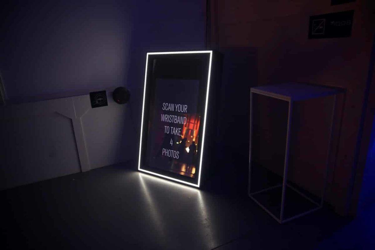 A screen with a white strip of white light around its edges invites users to "scan your wristband to take 4 photos."