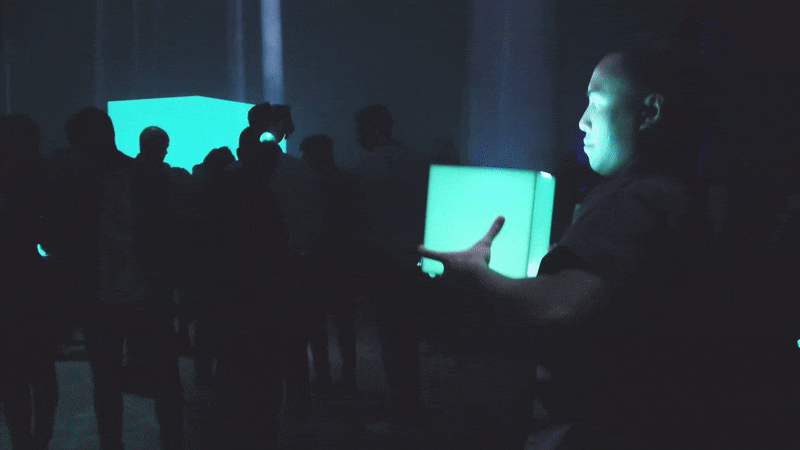 People crowd in a hall holding light cubes in their hands