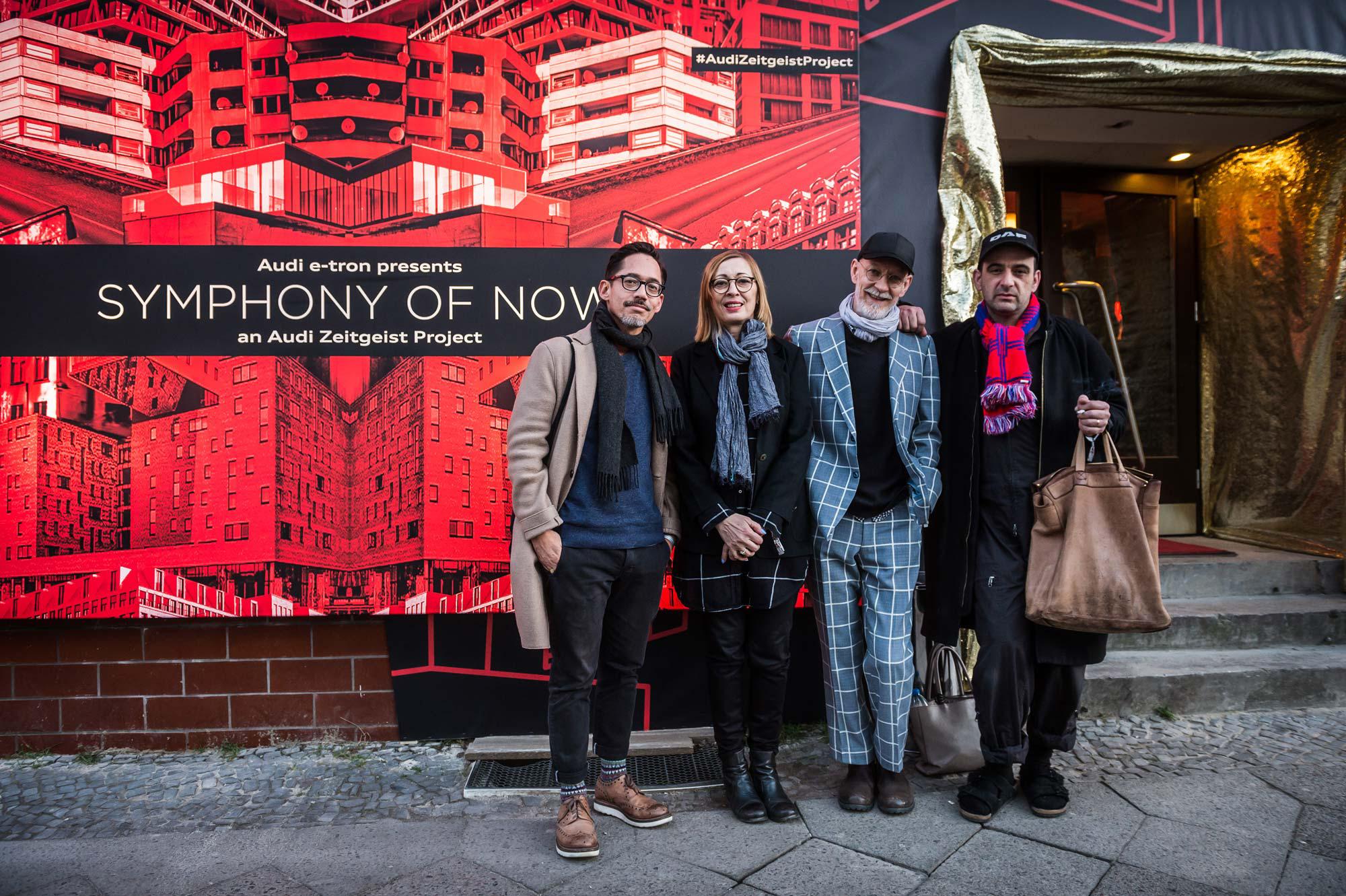4 musicians stand in front of the Symphony of Now poster outside the premiere.