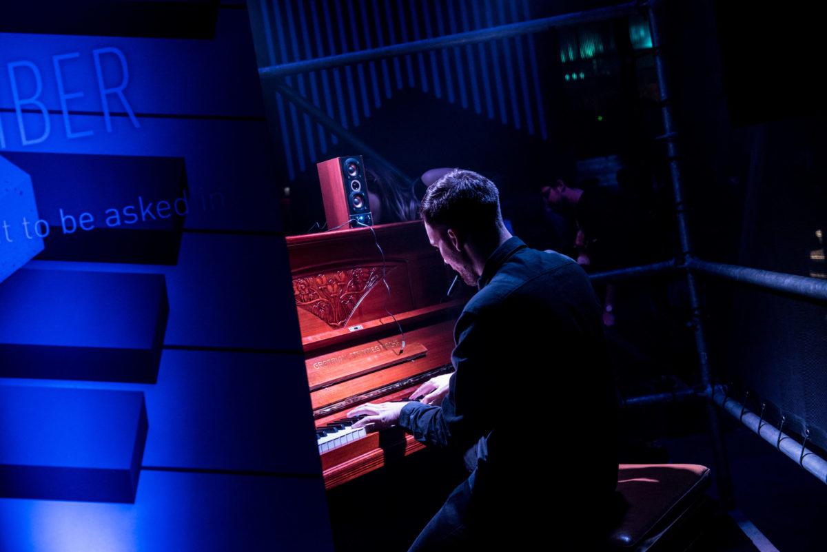 A pianist plays in a blue lit club environment.