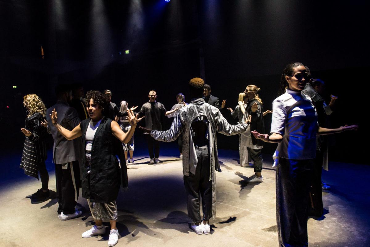 Professional dancers perform in a circle in a club environment under a stark spotlight.