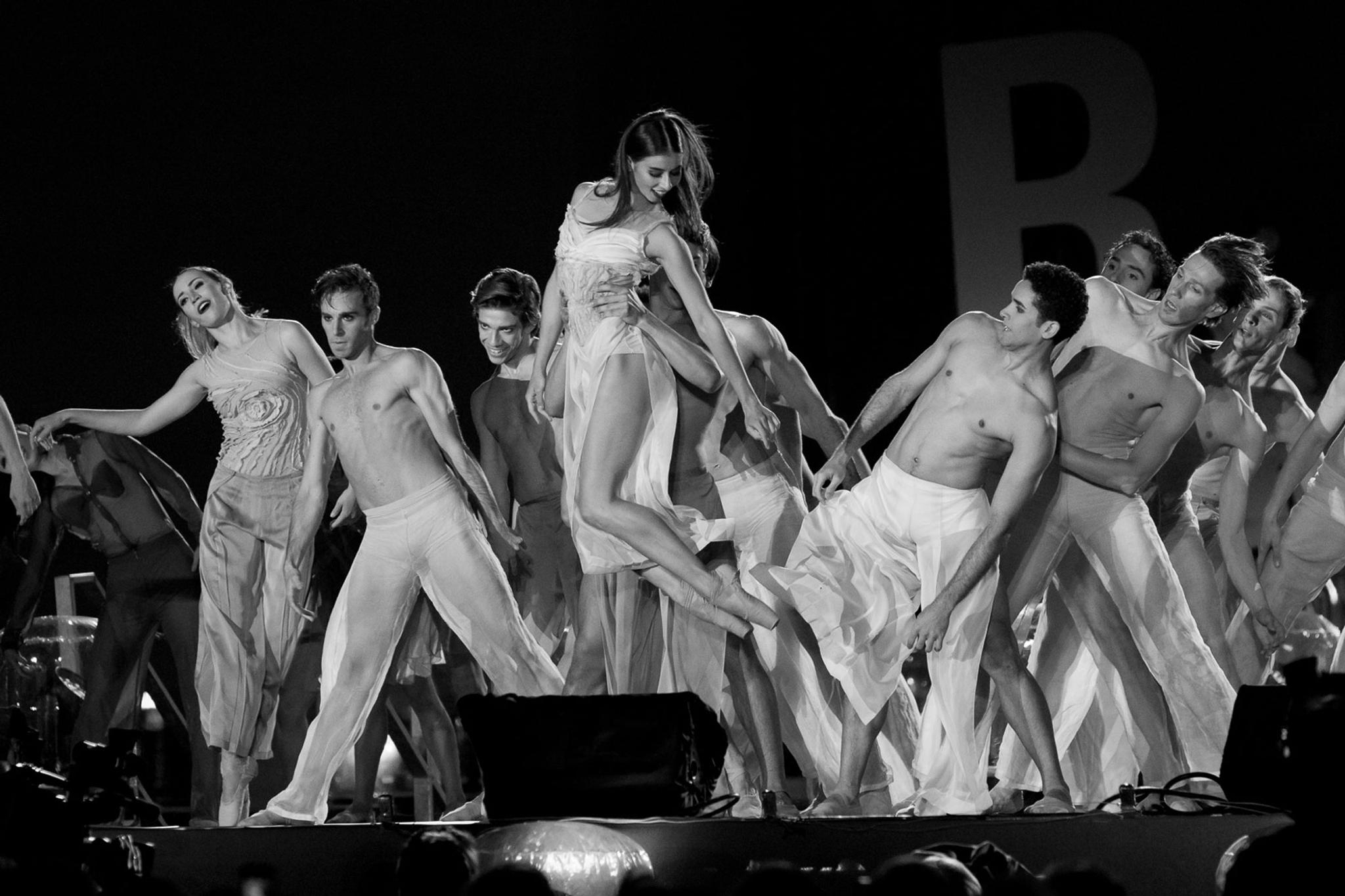 A black and white photo of a group of dancers. One lifts another up by the waist.