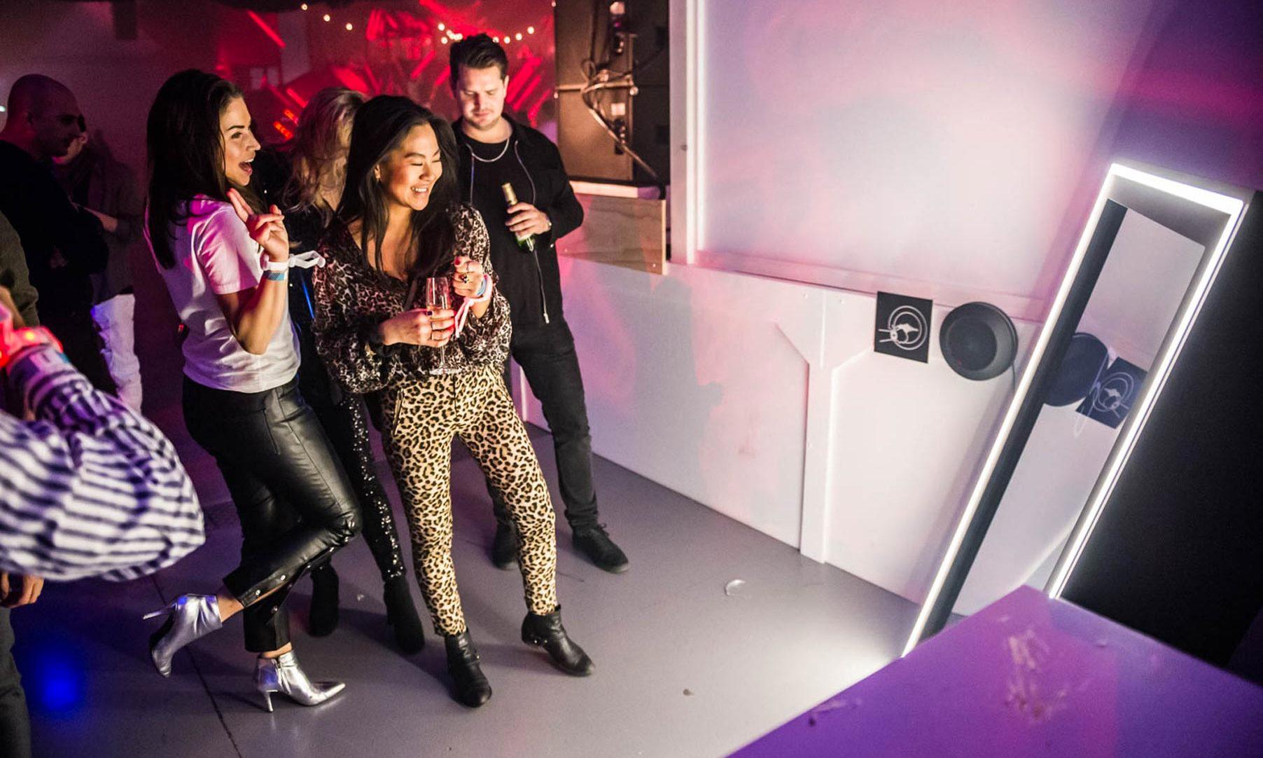 Partygoers take pictures in a mirror photo booth lined with bright white LED lights.