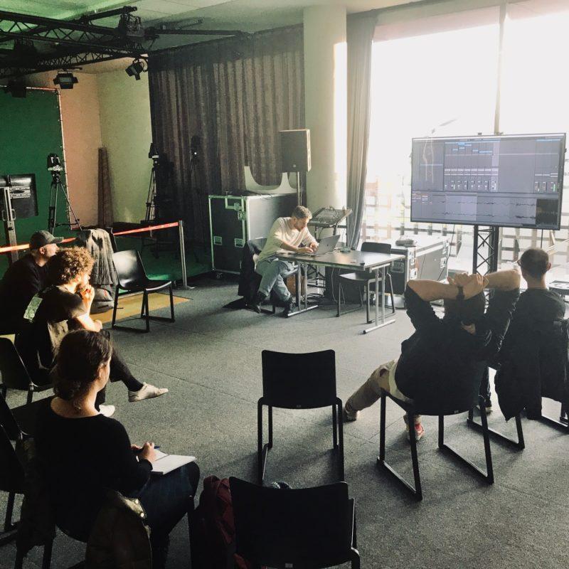 A music producer shows an ableton window to a group sitting in chairs.