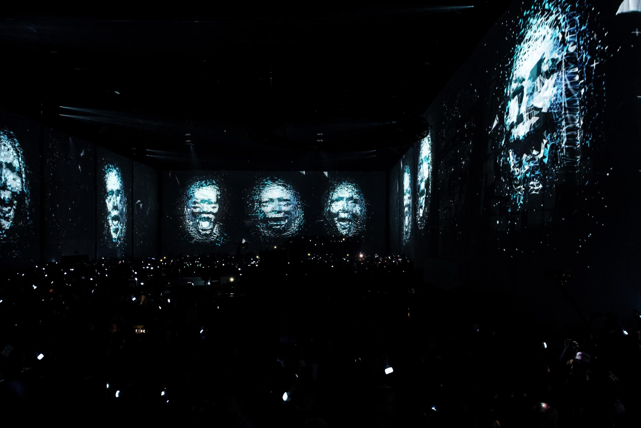 Projection mapping of faces cover the walls of a club environment.