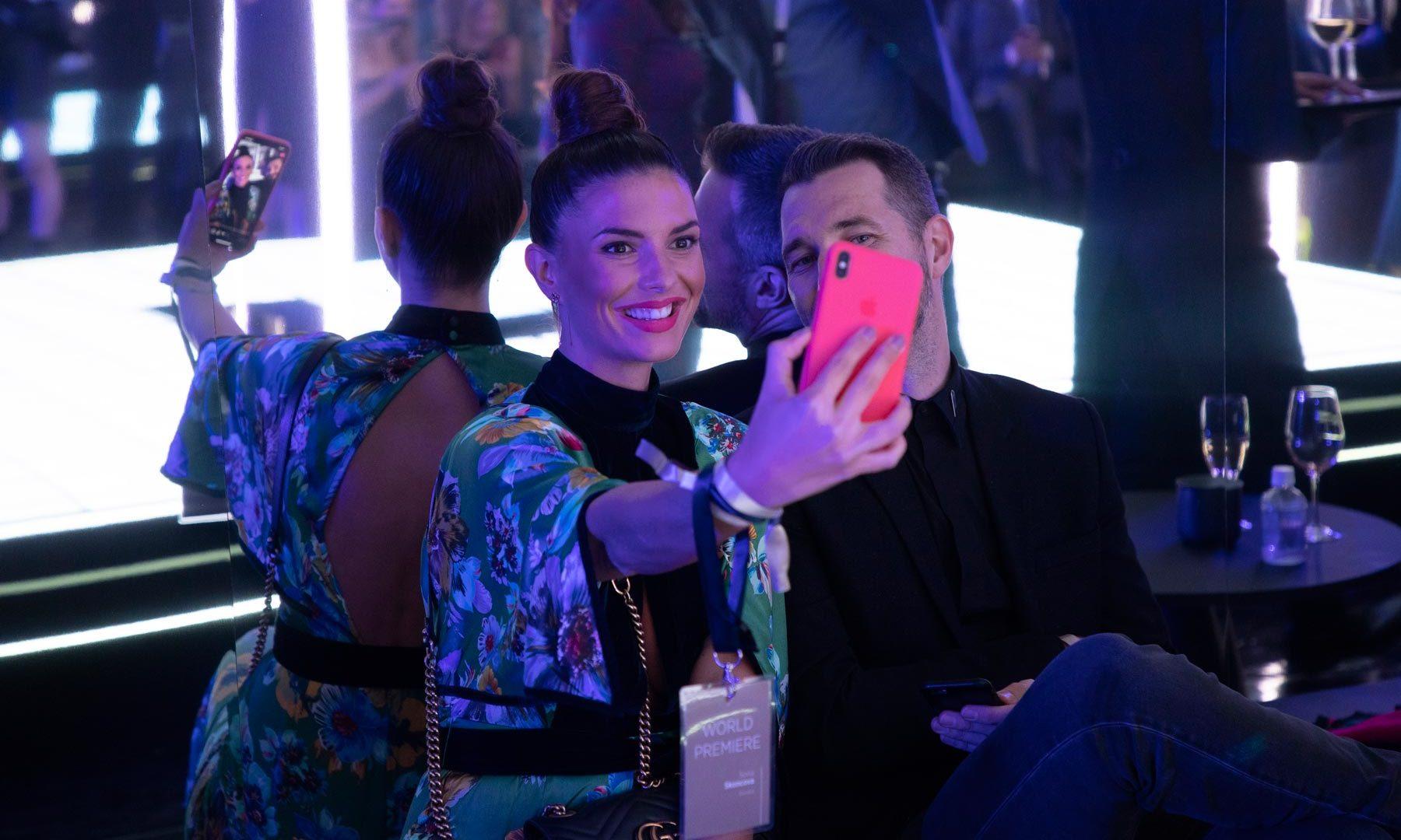 A man and a woman in chic evening wear take a selfie together.