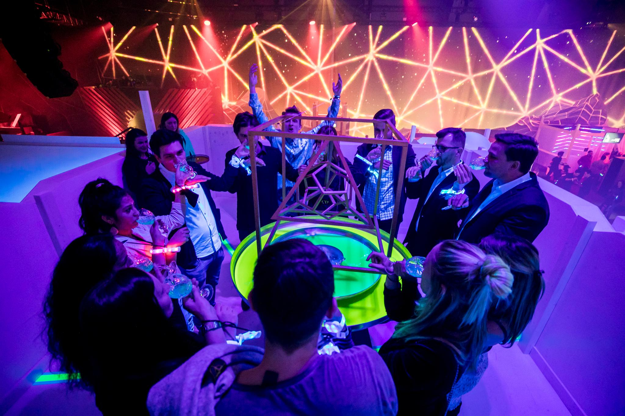 Friends around a table with a geometric sculpture in the center have drinks in a club environment.
