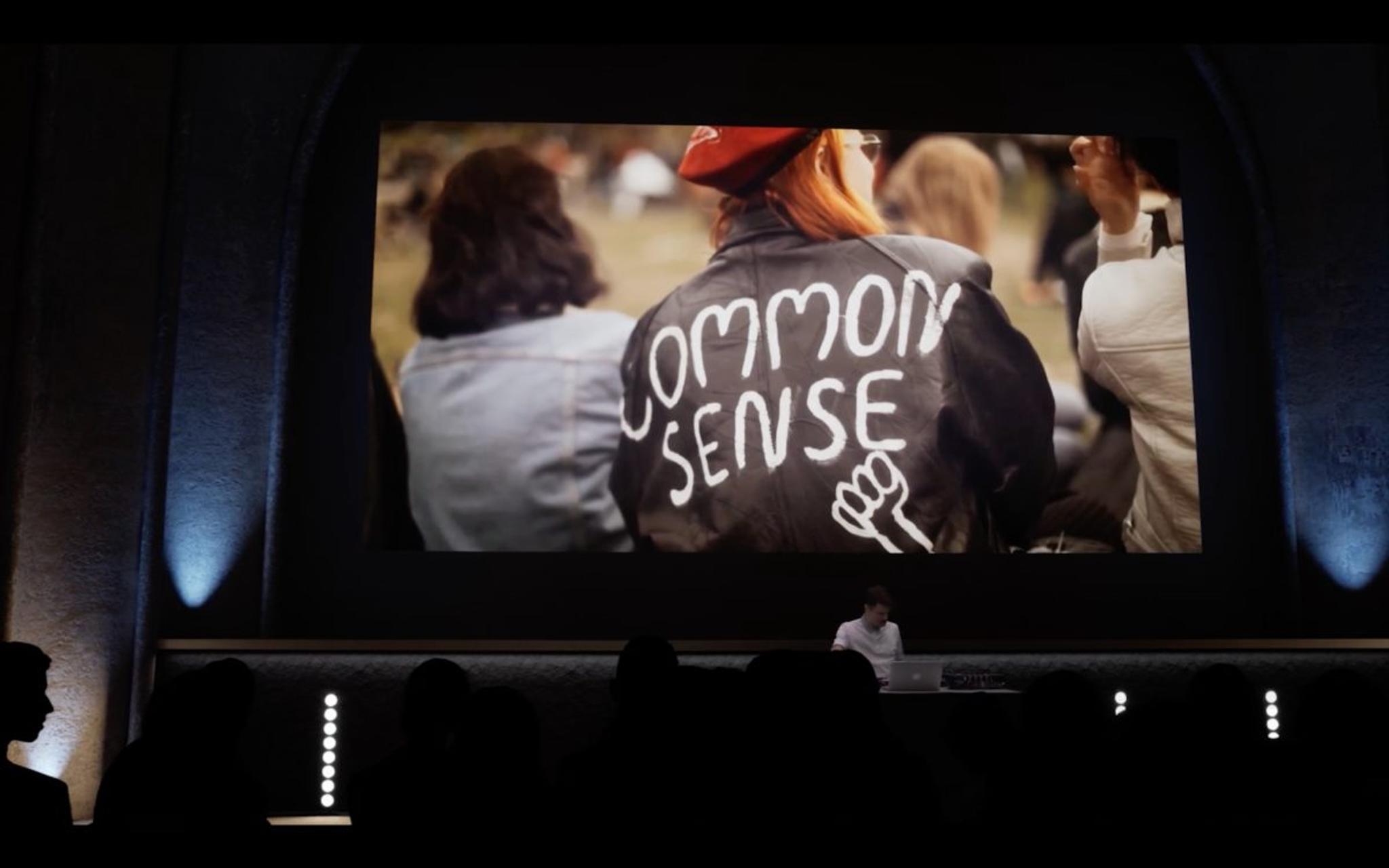 A digital rendering of a Symphony of Now screening accompanied by Alex.Do where an image of a person wearing a leather jacket with "common sense" written on the back is on the screen.