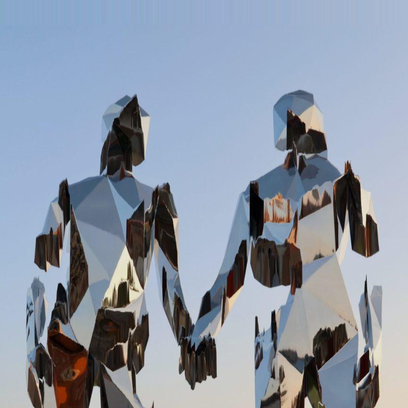 Two anthropomorphic geometric chrome figures hold hands against a dusky blue sky.