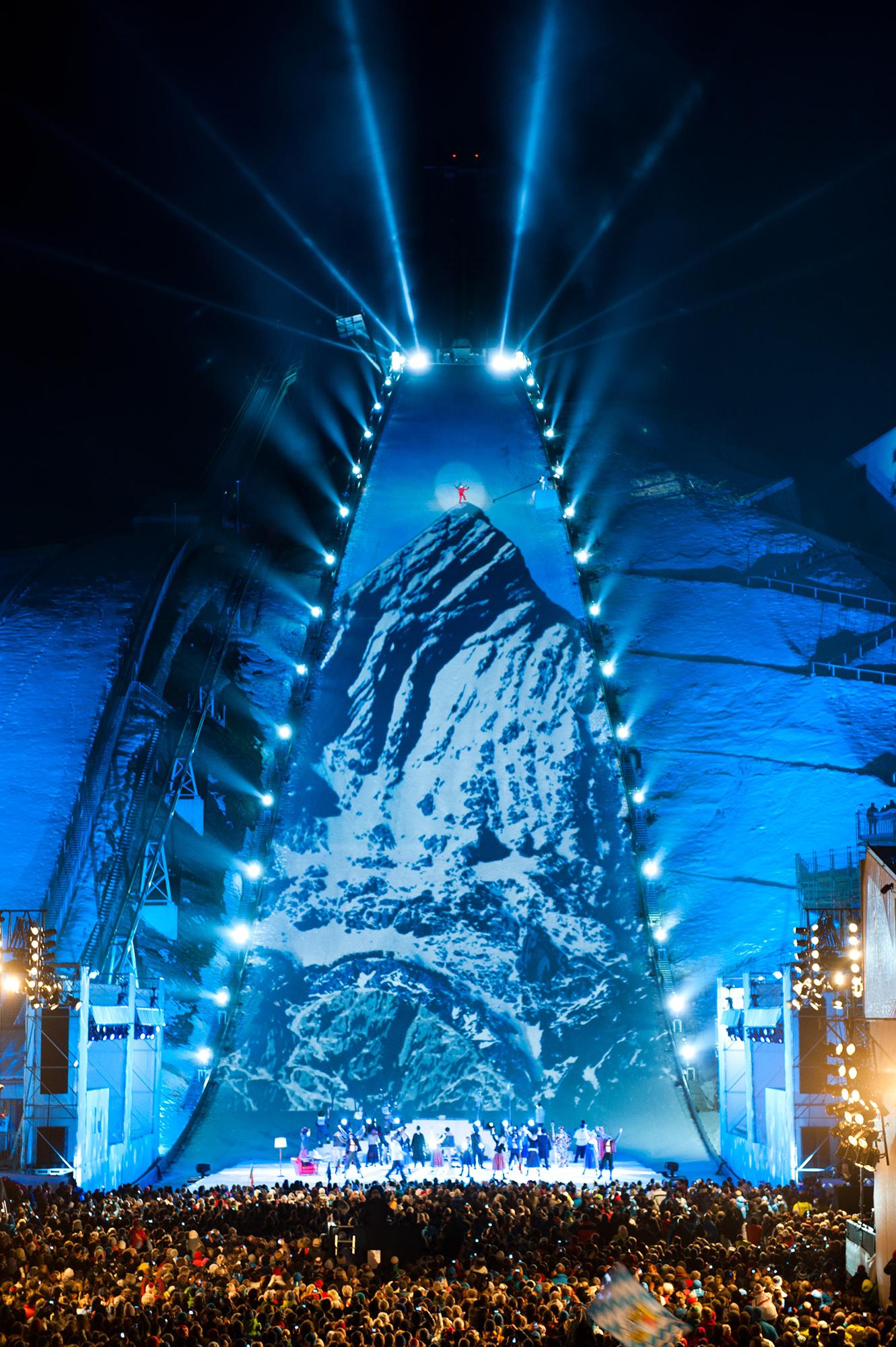 A mountain is projection mapped onto the ski slope as a sea of people looks on.