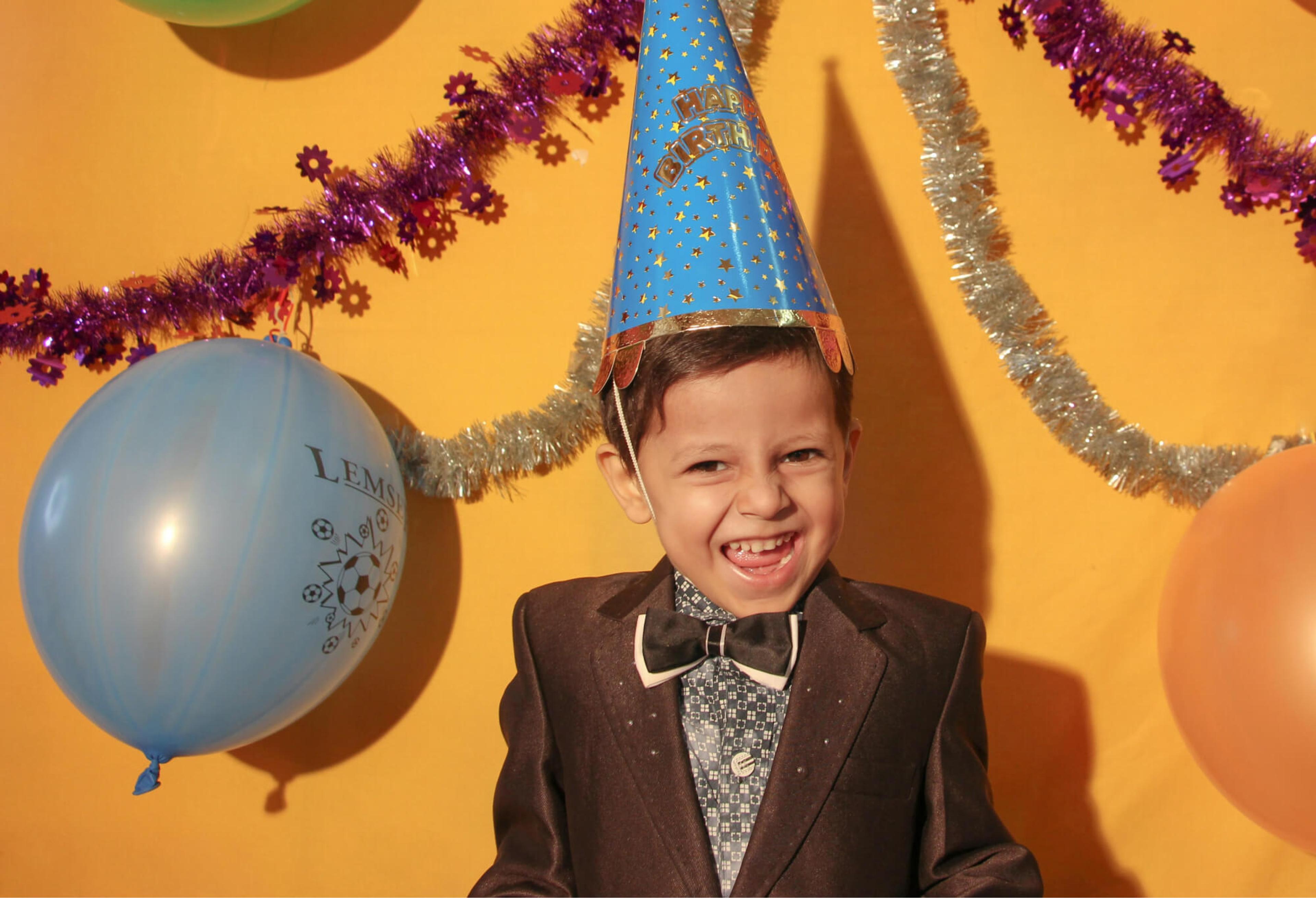 A young boy wearing a brown suit and a bow tie celebrates a birthday party.