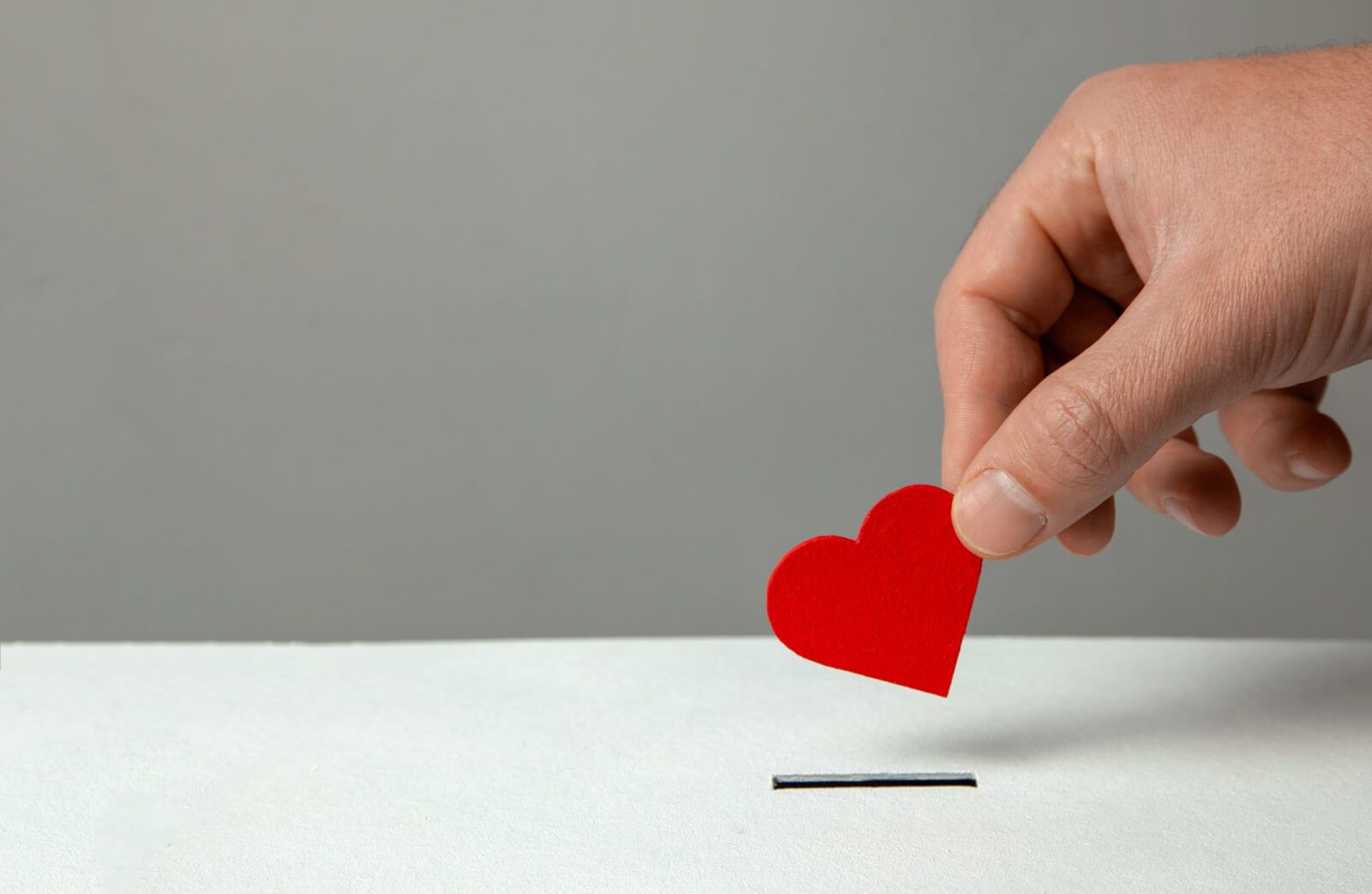 A hand holding a small paper heart prepares to insert it into a slot.