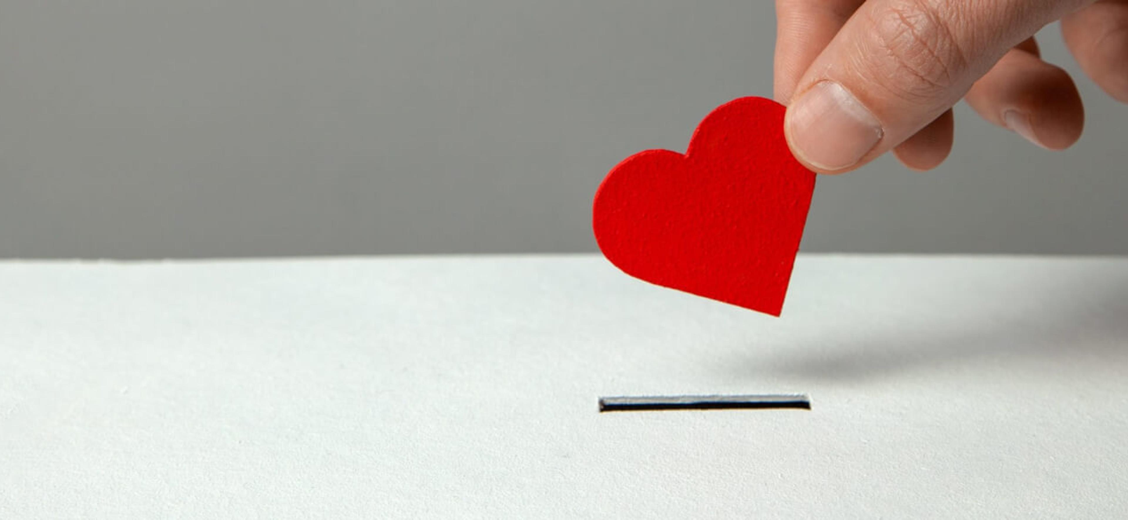 A hand holding a small paper heart prepares to insert it into a slot.
