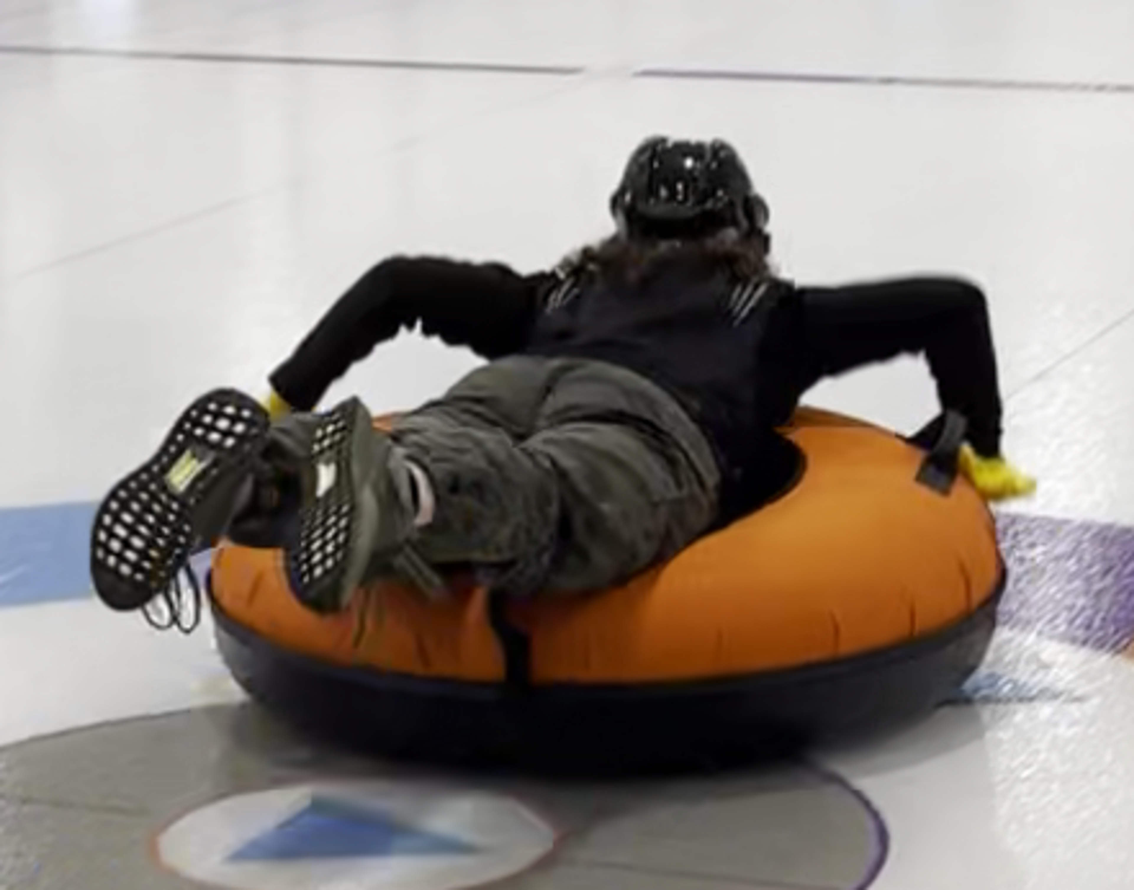 A grown person lying on a round tube sliding the curling ice.
