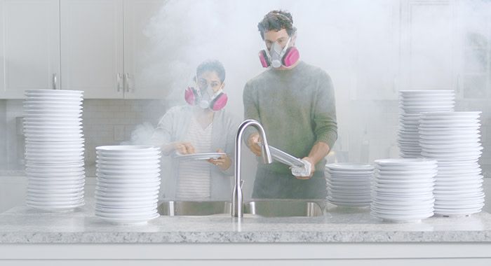 A man and a woman wearing respirators washing dishes with a lot of smoke surrounding them in a kitchen