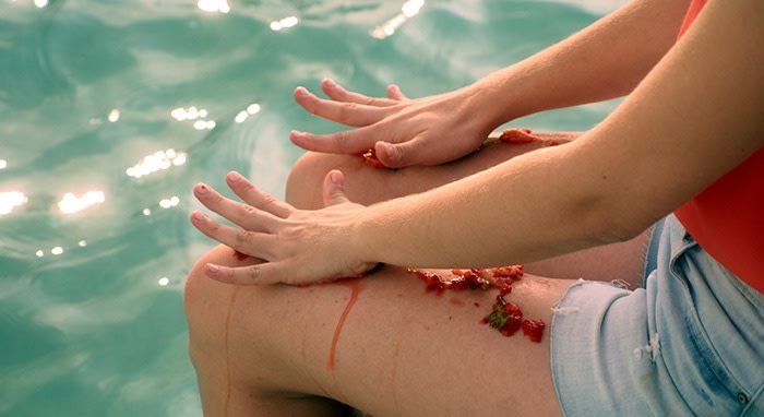 Woman sitting on the edge of the pool smashing strawberries on her thighs