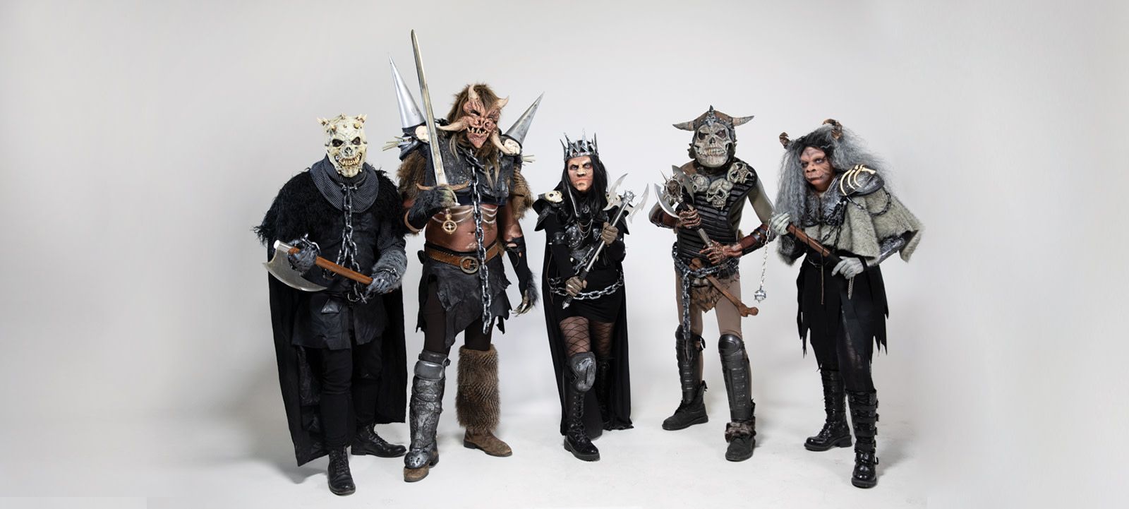 five people in monster costumes holding weapons in a white room