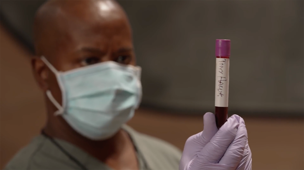 Doctor with surgical mask holds a vial of Tony Hawk's blood close to the camera