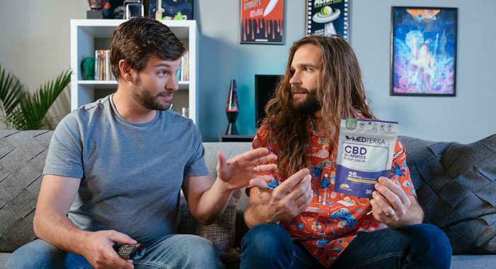 two guys sit on the couch and one reaches over to take medterra cbd gummies out of his hand