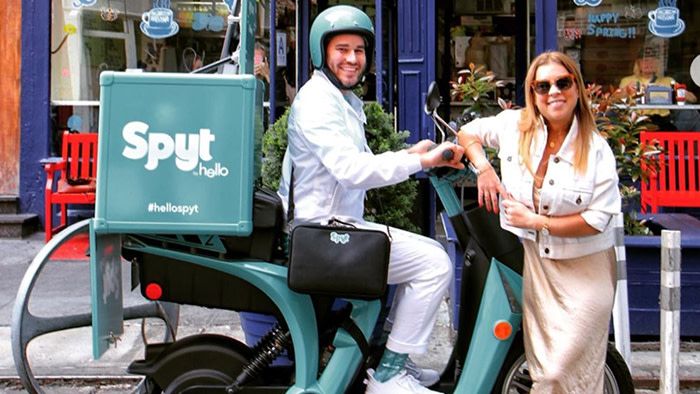 A man sits on the spyt hello mobile teeth brushing station scooter and a woman leans on the front of the scooter