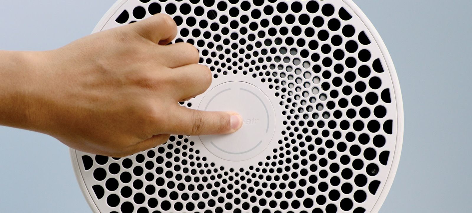 a downward shot of the top of a blueair air purifier with a hand pushing the middle of the fan