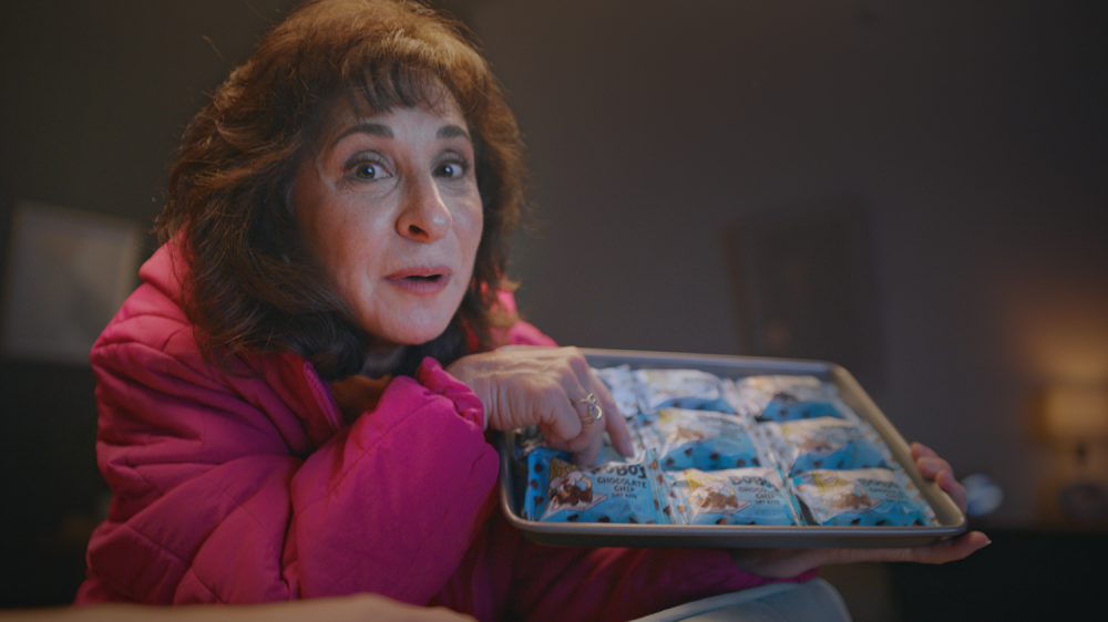 mother with puffy pink jacket holding and pointing to a tray of bobo's