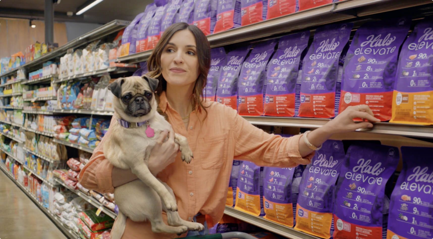 A woman shopping for Halo pet food carrying a calm pug in one arm