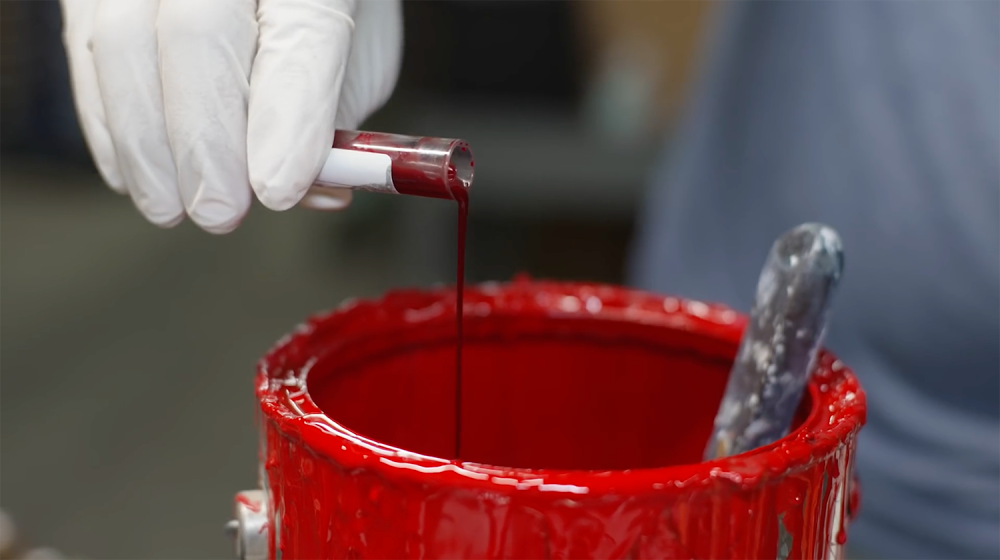 A close up shot of a vial of blood being poured into a can of red paint