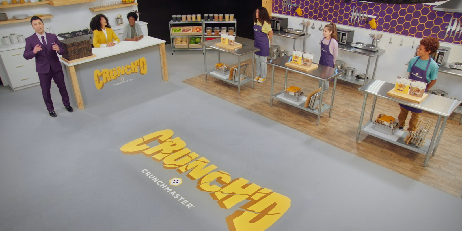 a wide shot of the crunched cruchmaster gameshow kitchen with the contestants behind their tables