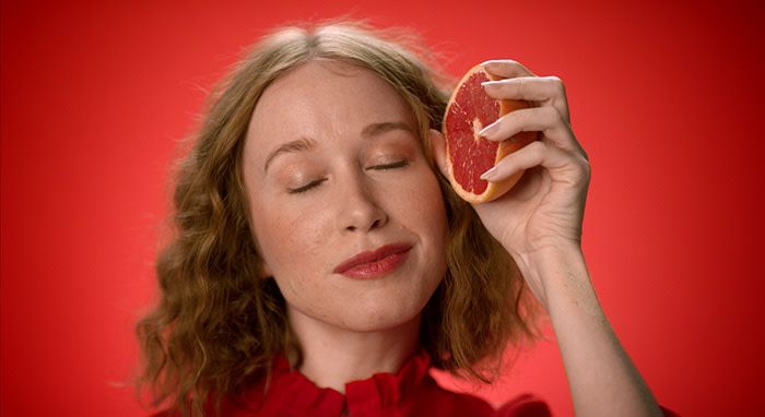 A close up shot of a woman holding a grapefruit up to her face with her eyes closed