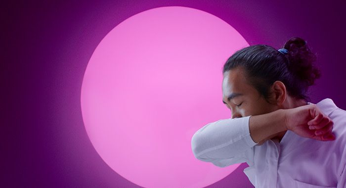 a man sneezing into his elbow with a pink illuminated circle in the background